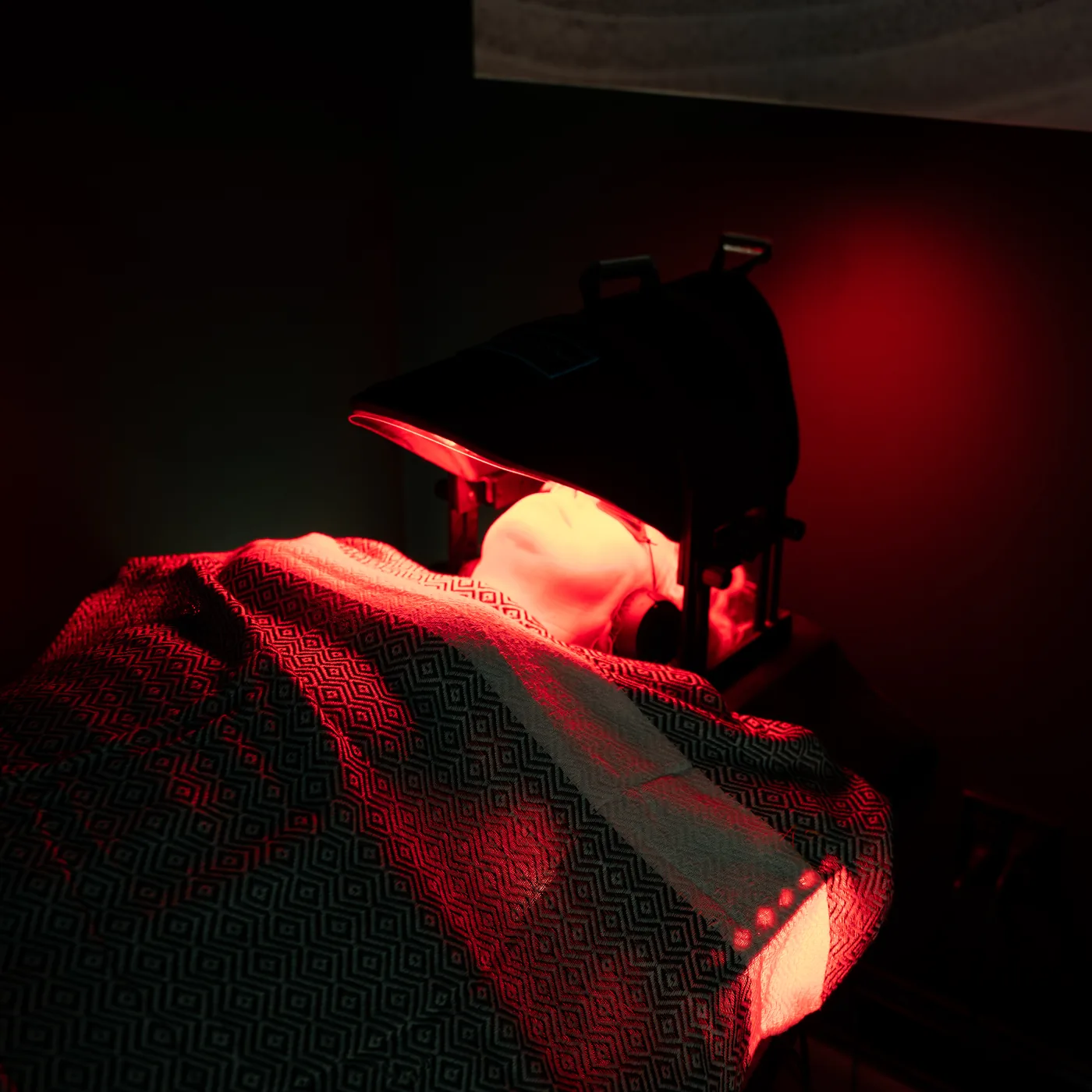 A member lying under the glowing red light canopy at Red Light Method Commack, covered by a patterned sheet in a darkened room