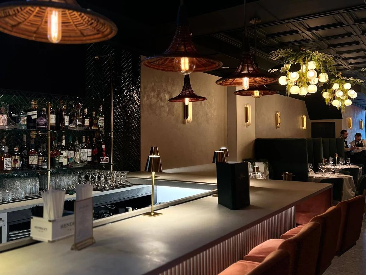 The bar at Casa Stellina in Farmingdale, with rattan pendant lights, a stocked back bar and terracotta velvet stools